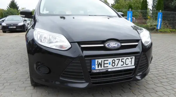Czarny Ford Focus 2011 z tablicą WE 875CT zaparkowany na kostce brukowej.
