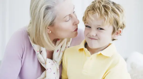 Una nonna bacia un bambino sorridente. Nonostante la tenerezza, i bambini non si baciano sempre, ma questo momento è speciale.