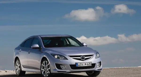 Srebrna Mazda 6 2.0 benzyna na tle błękitnego nieba z chmurami.