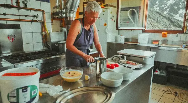 Une femme prépare des ingrédients dans une cuisine de montagne, un aperçu de son quotidien à travailler dans un refuge.