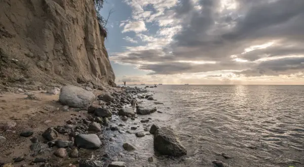 Klif w Gdyni, kamienista plaża i morze. W oddali widać statki. To jedna z pięknych gdynia atrakcji.