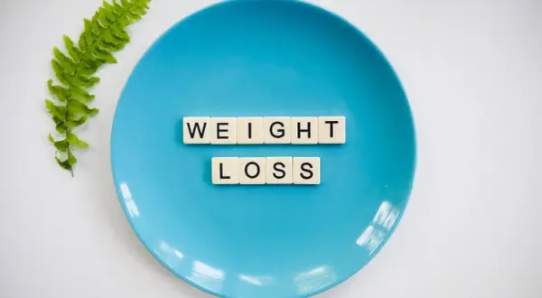 Niebieski talerz z literami "WEIGHT LOSS" i gałązką paproci. Czy to znak, że za mało kalorii na redukcji?