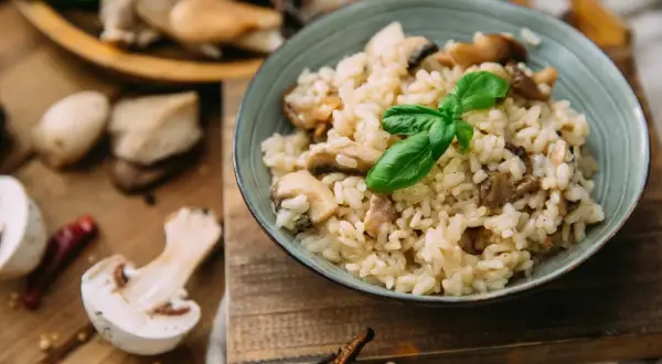 Kremowe risotto z grzybami, ozdobione listkiem bazylii. Pyszny ryż włoski w misce, otoczony świeżymi grzybami i papryczką chili.