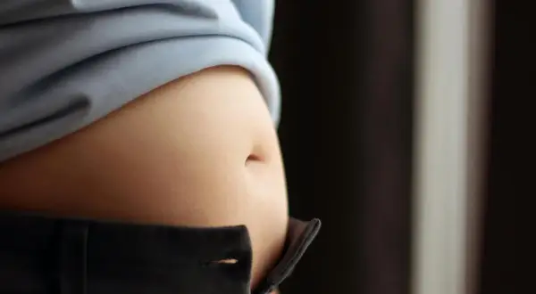 En svullen mage, kanske gravid, syns under en ljusblå tröja och över ett par mörka byxor.