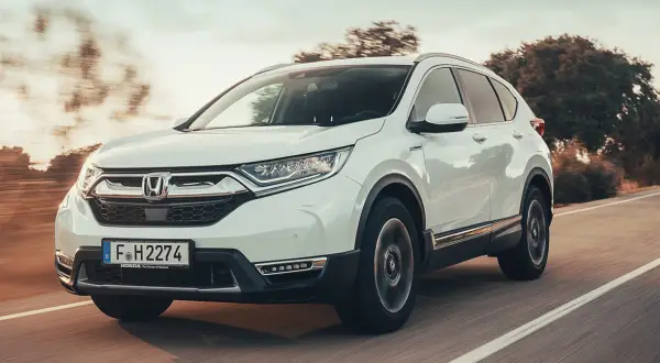 Biała Honda CRV 2025 pędzi po drodze, otoczona rozmazanymi drzewami i słońcem.