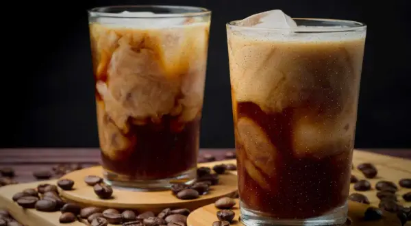 Två glas med krämigt iskaffe, perfekt för ett enkelt iskaffe recept. Kaffebönor sprider sig runt glasen.