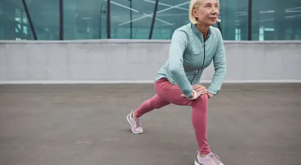 Donna bionda in abiti sportivi fa stretching, contrastando l'atonia muscolare con un affondo.