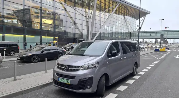 Szary van czeka na pasażerów przed nowoczesnym terminalem lotniska. Może to być transport z Koszalina do Gdańska.