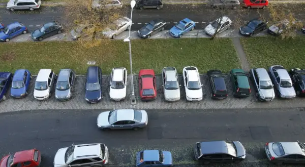 Wiele samochodów zaparkowanych pod blokiem, przypominające o przepisach parkowania.