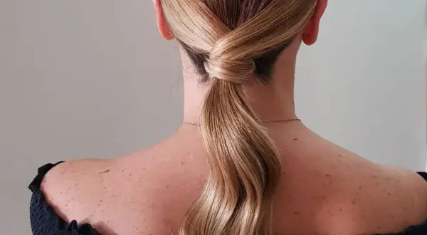Capelli biondi raccolti in una coda bassa con un'elegante torsione, perfetta per una cerimonia.