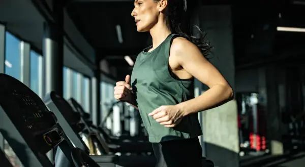 Eine Frau läuft auf einem Laufband im Fitnessstudio. Sie trainiert intensiv und zeigt, was ein Laufband für die Ausdauer bringt.