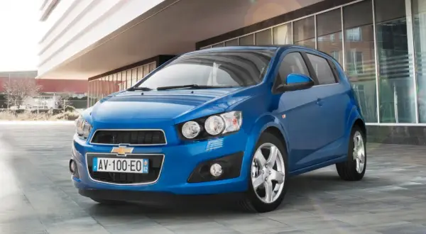 Błękitny Chevrolet Aveo stoi przed nowoczesnym budynkiem.