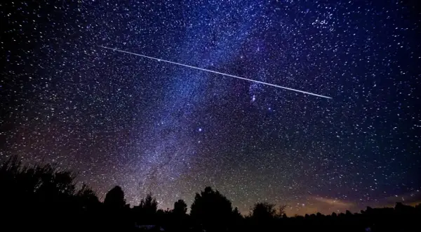 Una estrella fugaz cruza el cielo nocturno estrellado, ideal para ver las Perseidas en Madrid.