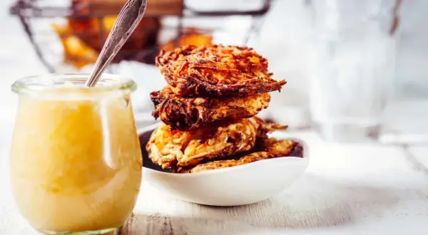 Goldbraune Kartoffelpuffer stapeln sich in einer Schüssel, daneben ein Glas Apfelmus. Ein perfektes Kartoffelpuffer Rezept für jeden Anlass.