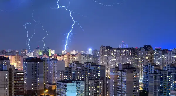 Grzmoty nad miastem, błyskawice rozświetlają nocne niebo. Warto pomyśleć o ubezpieczeniu od przepięć, by chronić swój dom.