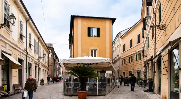 Una donna passeggia nel centro di Senigallia, tra palazzi color pastello e un dehors con palma.