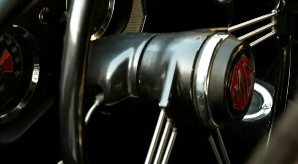 Wnętrze klasycznego MG. Kierownica z chromowanymi szprychami i emblematem MG. Słychać metaliczny pisk przy skręcaniu.