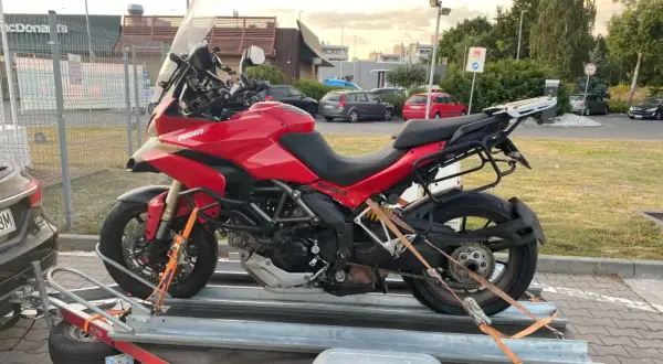 Czerwony motocykl Ducati na przyczepie, zabezpieczony pasami.