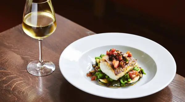 Piatto di pesce con verdure e un bicchiere di ribolla gialla.