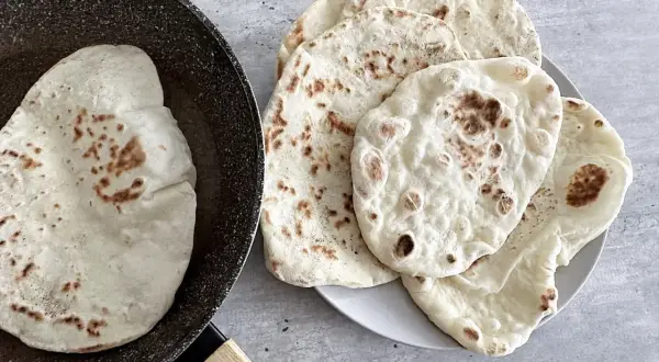 Chlebek naan przepis: świeżo usmażone placki na patelni i talerzu, gotowe do podania.