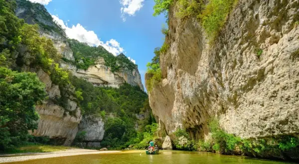 Wąwóz Gorges du Tarn, zielona rzeka i łódź z wioślarzami wśród skalnych ścian porośniętych bujną roślinnością.