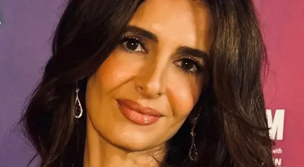 Amal Clooney, con su cabello oscuro y pendientes brillantes, sonríe ante la cámara.