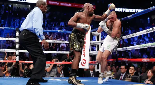 A referee watches as Floyd Mayweather Jr. lands a punch on Conor McGregor during their boxing match.
