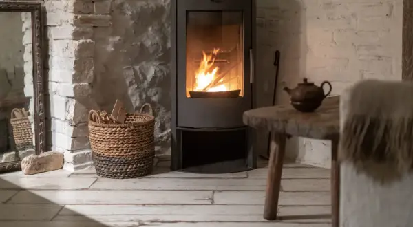 Un poêle à bois moderne diffuse une chaleur réconfortante, parfait pour un chauffage central cosy. Une théière ancienne et un panier de bois complètent l'ambiance rustique.