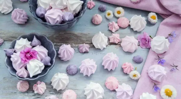 Zarte Baisers in Rosa, Lila und Weiß, perfekt für ein süßes Baiser Rezept. Kleine Blumen schmücken die Leckereien.