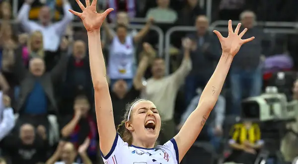 Karolina Drużkowska z uniesionymi rękami, krzyczy z radości na meczu siatkówki.
