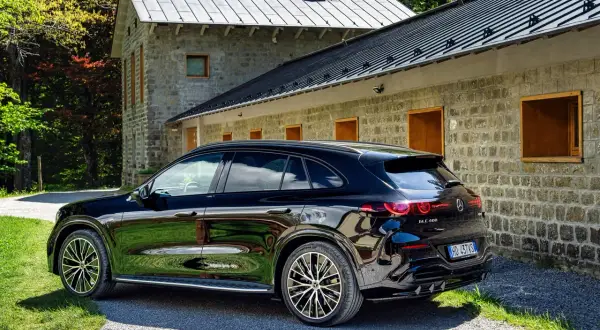 La nuova Mercedes GLC 2026 nera lucida parcheggiata davanti a una casa in pietra con tetto grigio, immersa nel verde.