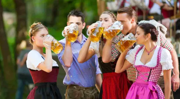 Cinco amigos brindan con jarras de cerveza, celebrando cuando es Oktoberfest con trajes bávaros tradicionales.