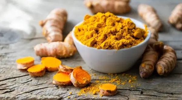 Kurkuma-Wurzeln und Pulver auf Holz. Informiert über die Frage: wieviel curcumin pro tag.