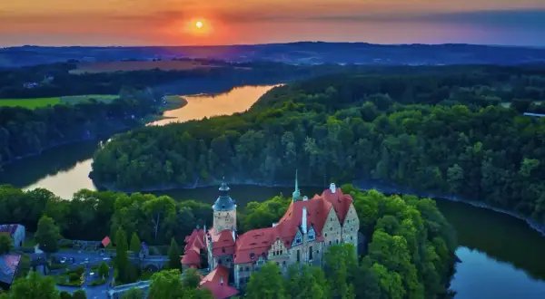 Malowniczy zamek otoczony lasami nad jeziorem, zachód słońca nad wzgórzami. Ten piękny most w Czechach wygląda jak z bajki.