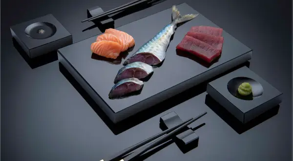 Sashimi-Zutaten: Lachs, Thunfisch, Makrele, Wasabi und Stäbchen. Die Frage "aus welchem Land kommt Sushi" führt uns nach Japan.
