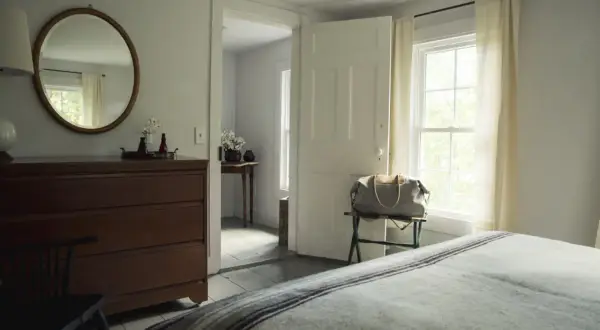Ein runder **Spiegel im Schlafzimmer** hängt über einer Kommode. Ein Koffer steht bereit, die Tür ist offen.