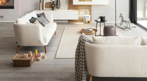 Gemütliches Wohnzimmer mit einem cremefarbenen Sofa vor bodentiefen Fenstern. Ein Kaminfeuer wärmt den Raum.