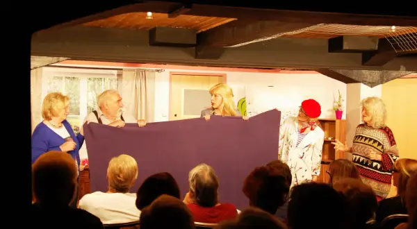 Schauspieler des losemund theater halten ein lila Tuch, während sie vor einem Publikum auftreten.