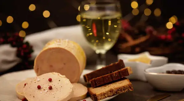 Un délicieux bloc de foie gras tranché, servi avec du pain d'épices et un verre de vin blanc, le tout dans une ambiance festive.