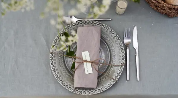 Vackert dukat bord med en lila servett vikt som en blomma, knuten med snöre. En liten lapp med texten "...when the weather is hot" sitter fäst.