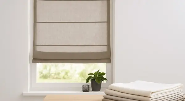 Ein beiger Raffrollo mit Vorhang kombinieren? Hier ist ein Beispiel: Ein schlichtes Raffrollo über einem Fenster, daneben ein Stapel Stoffe in verschiedenen Grautönen.
