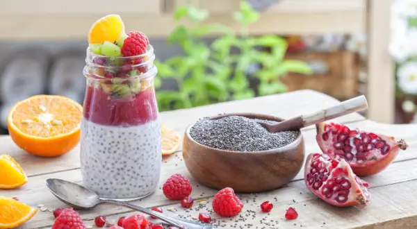 Un délice fruité : un pot de pudding de chia garni de fruits rouges, kiwi et orange, à côté d'une coupelle de graine de chia bienfait.