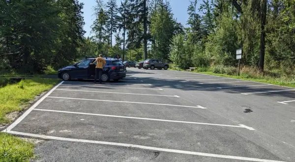 Parking przy szlaku na przełęcz Szarcula. Kilka samochodów na nowym, asfaltowym parkingu otoczonym lasem.