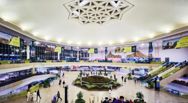 Wnętrze lotniska, które może być największym lotniskiem na świecie, z wielopoziomowymi galeriami, schodami ruchomymi i centralną zieloną przestrzenią.