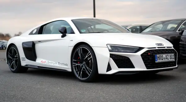 Białe Audi R8 V10 z napisem "Audi Zentrum Rostock" na progu, zaparkowane na zewnątrz.