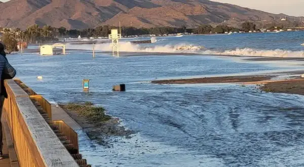 El espigón Garrucha bajo el agua, con olas rompiendo y montañas al fondo.