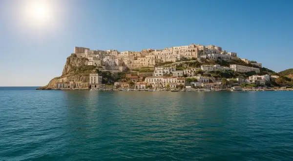 La spiaggia La Cala di Peschici, con le sue case bianche aggrappate alla roccia, si specchia nel mare blu sotto un sole splendente.