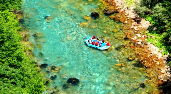 Rafting na turkusowej rzece w kanionie rzeki Tara. Grupa turystów w kamizelkach ratunkowych płynie pontonem po krystalicznie czystej wodzie.