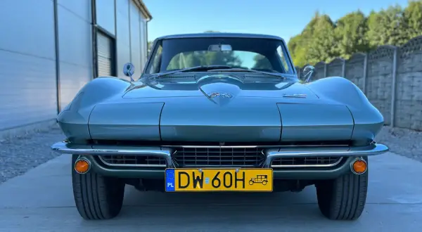 Klasyczny zielony Corvette C2 z lat 60. stoi przed nowoczesnym budynkiem.