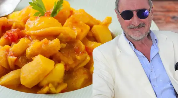 Un hombre con gafas de sol y traje blanco sonríe junto a un plato de papas con choco de la abuela, un guiso casero.